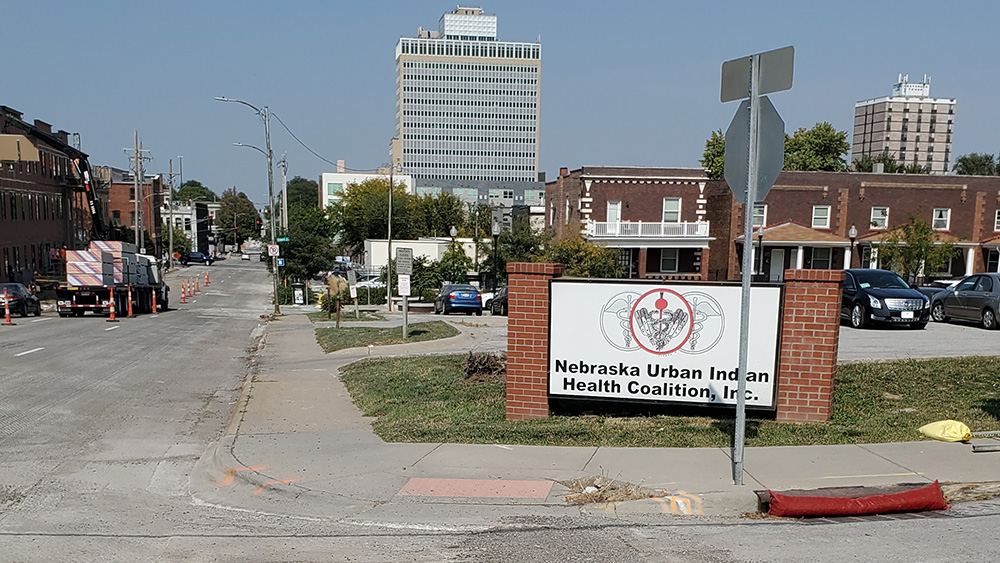 The Nebraska Urban Indian Health Coalition sign and building with parking lot in front and traffic lanes adjacent.